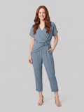 Lyra draped knot jumpsuit in dusty blue, wrap V-neck with knotted waist, front view on model